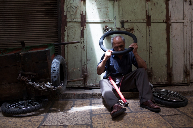 A man in the Old City sits on the ground fixing his tire for his cart. 