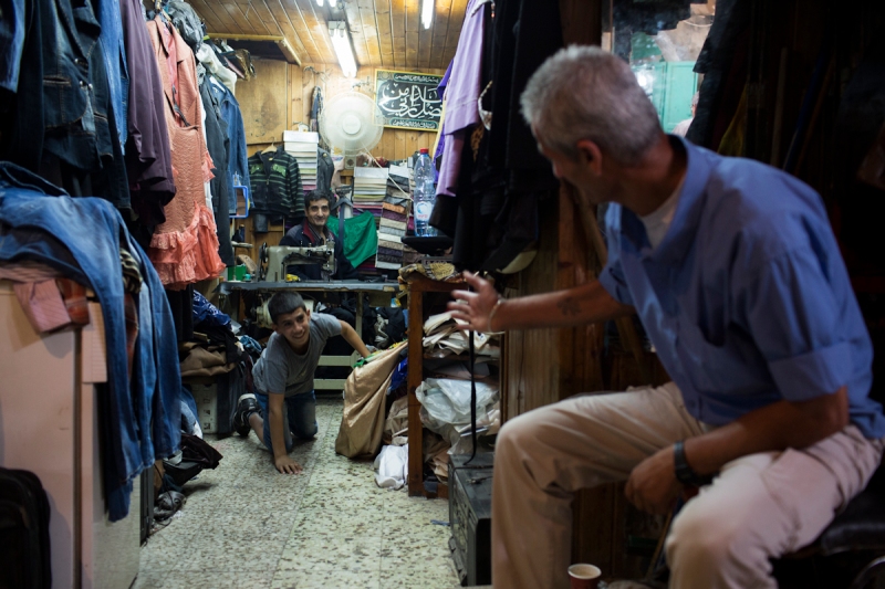 A man entertains a boy as he waits for his clothes to be fixed in the Old City.  